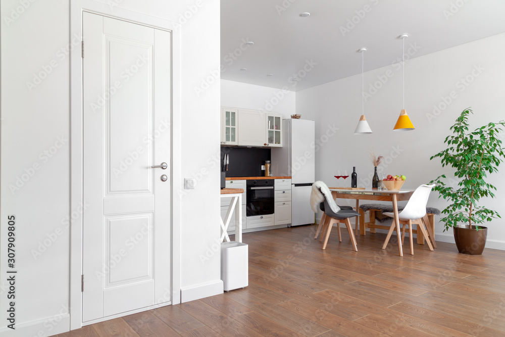 Modern interior of cozy kitchen, dining room, white furniture, wall, black accessories, natural materials, wooden chairs, green flower in pot. Concept scandinavian design apartment of young family Modern interior of cozy kitchen, dining room, white furniture, wall, black accessories, natural materials, wooden chairs, green flower in pot. Concept scandinavian design apartment of young family