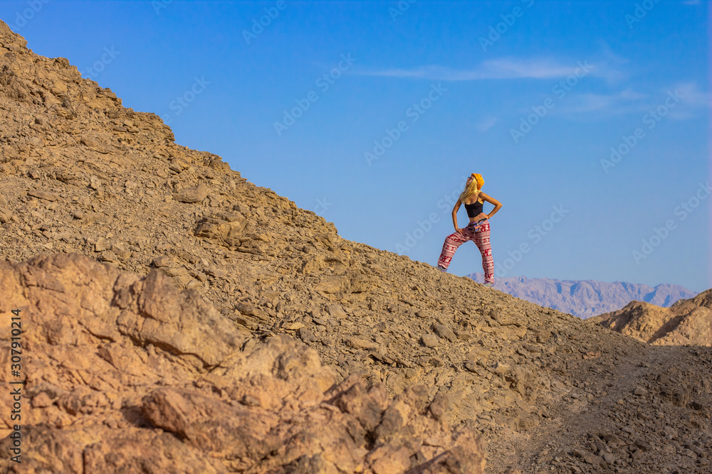 travel photography concept funny woman pose in happy mood on desert sand stone rocky mountain scenic landscape environment on empty blue sky background , copy space 