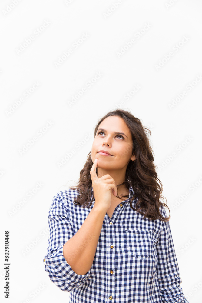 Thoughtful student girl touching chin and looking up at copy space. Young woman in casual checked shirt standing isolated over white background. Advertising concept Thoughtful student girl touching chin and looking up at copy space. Young woman in casual checked shirt standing isolated over white background. Advertising concept