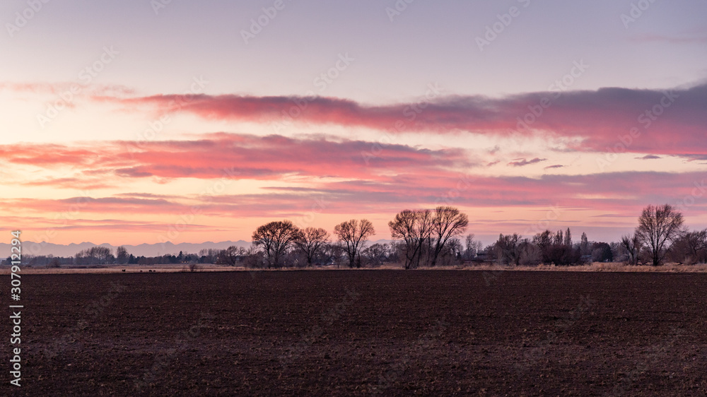 Red sunset with farm buildings and plowed field and distant mountains