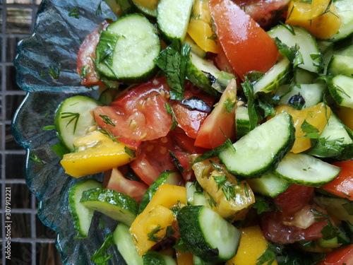 Vegetable salad of sliced yellow sweet pepper, tomatoes, dill, parsley, garlic, green onions and cucumber pieces. Seasonal food with plenty of vitamins, suitable for vegans and vegetarians.