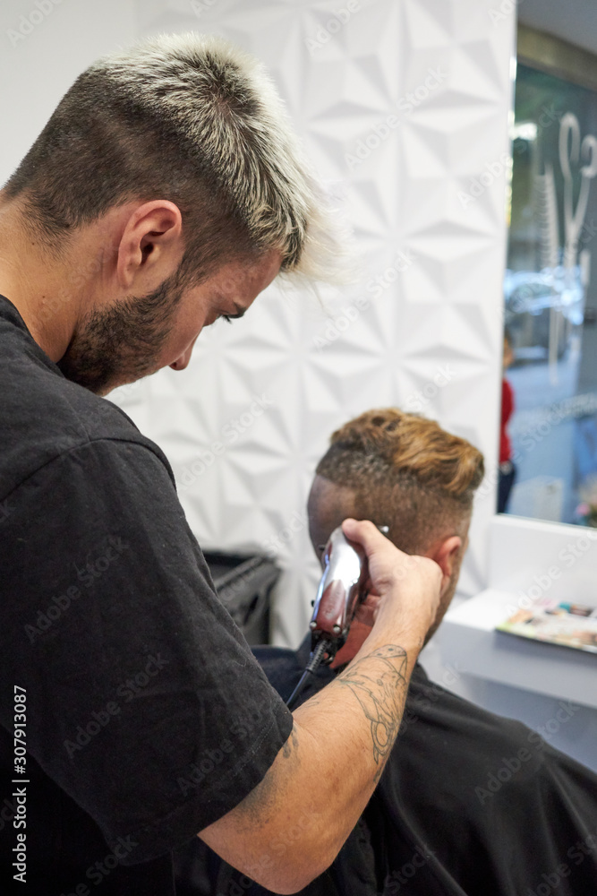 Fototapeta premium hairdresser cutting hair to man with electric razor
