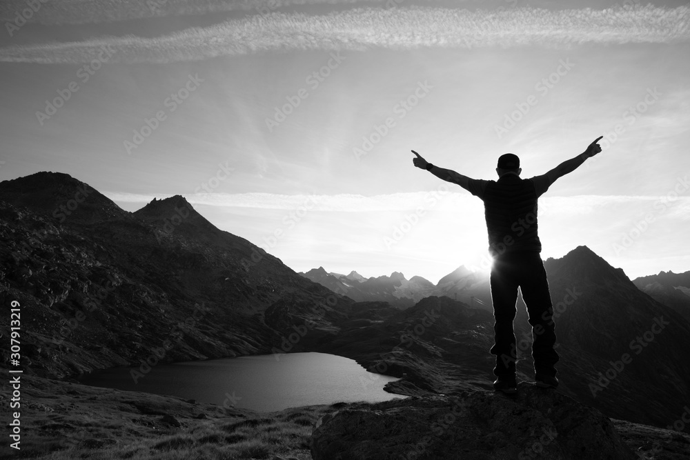 Hiker is standing on a rock with raised hands and enjoying sunrise in the Alps in Switzerland Hiker is standing on a rock with raised hands and enjoying sunrise in the Alps in Switzerland