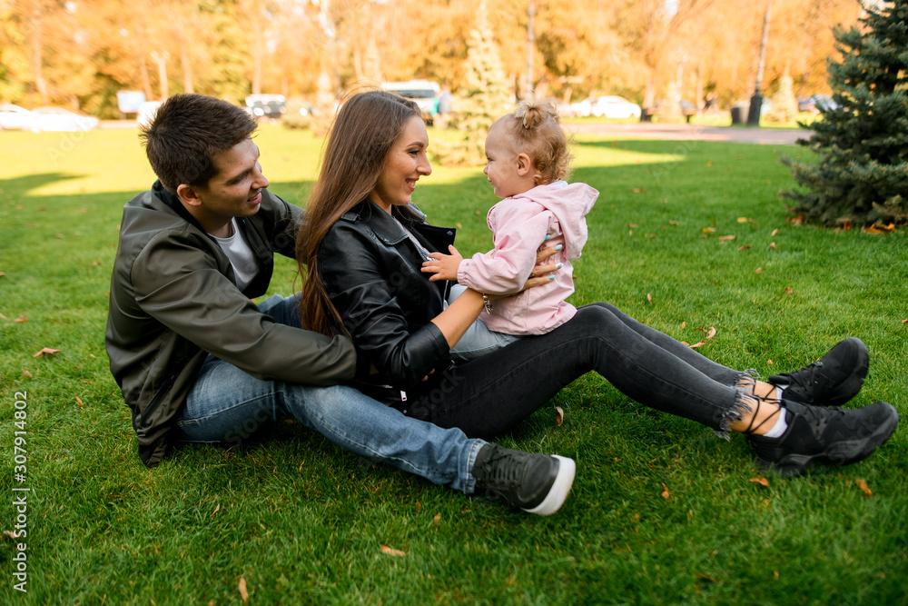 Happy family sitting on the green lawn with a baby on the mother knees