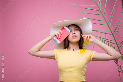 Beautiful girl in a huge white hat with a passport in her hands in glasses is going on a trip and rejoices in a yellow T-shirt and pink background