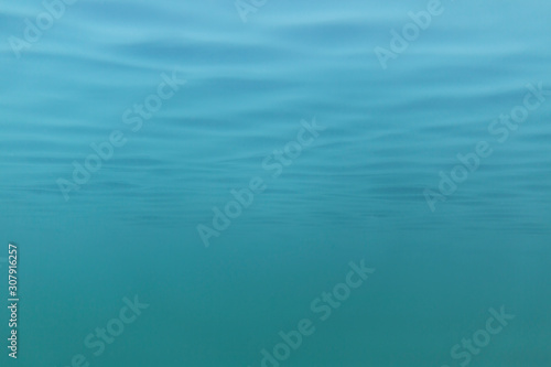 Picture of blue to green shades of water mass from under water. Fine structure of waves from below. Light blue to azure color transition.