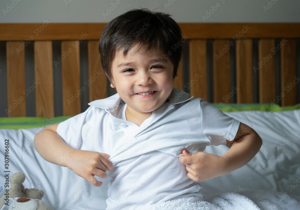 Foto Stock School boy sitting in bed and try to wearing his cloth with