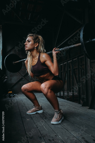 Young muscular woman doing barbell squat exercise in the gym. © Mihail