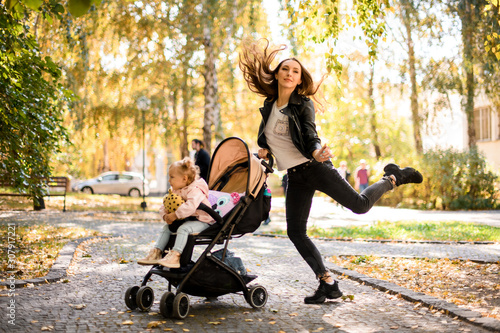 Cheerful mother jumping up holding a her daughter baby carriage