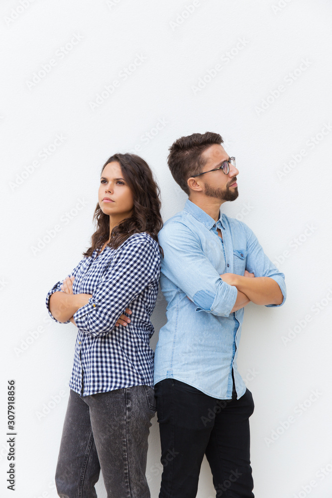 Sad unhappy couple standing back-to-back with arms crossed. Young woman in casual and man in glasses in glasses posing isolated over white background. Breakup concept Sad unhappy couple standing back-to-back with arms crossed. Young woman in casual and man in glasses in glasses posing isolated over white background. Breakup concept