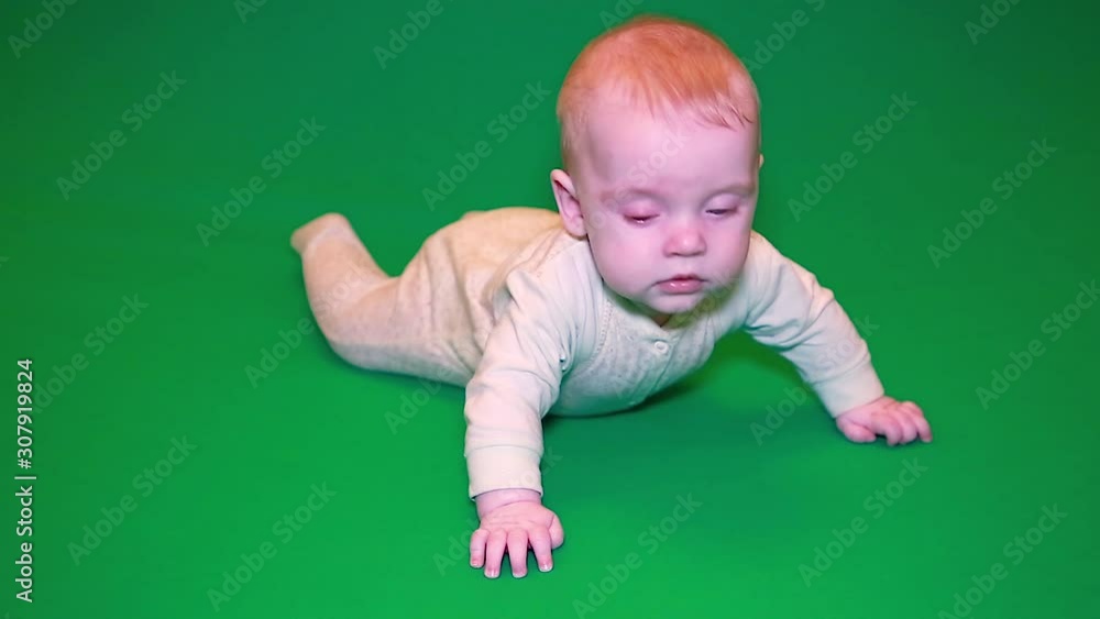 A newborn baby boy trying to crawl on the floor on a green screen . The concept of family happiness. Isolate the chroma key A newborn baby boy trying to crawl on the floor on a green screen . The concept of family happiness. Isolate the chroma key