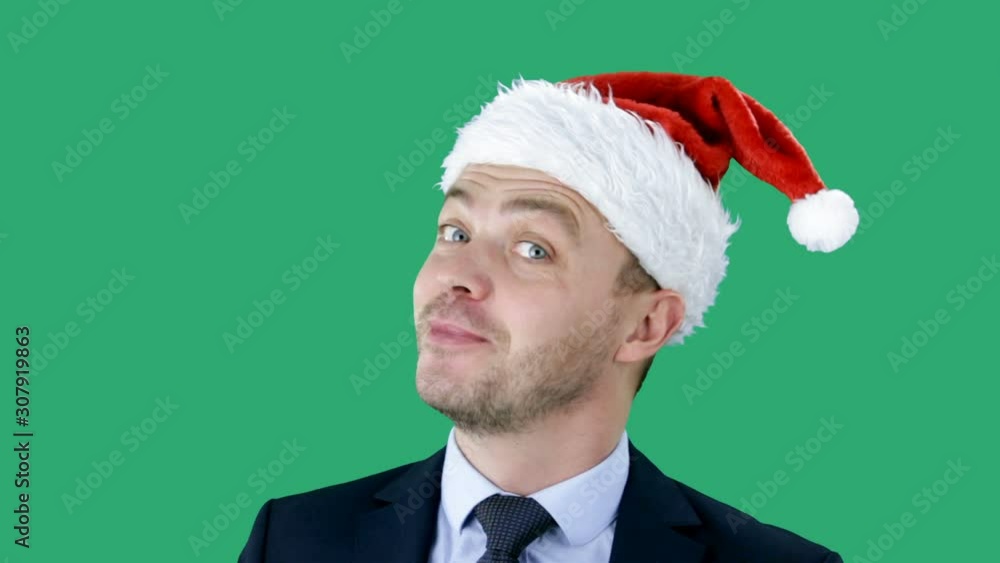 Young handsome caucasian guy in business suit and Santa hat stands on green background. Chroma key Young handsome caucasian guy in business suit and Santa hat stands on green background. Chroma key