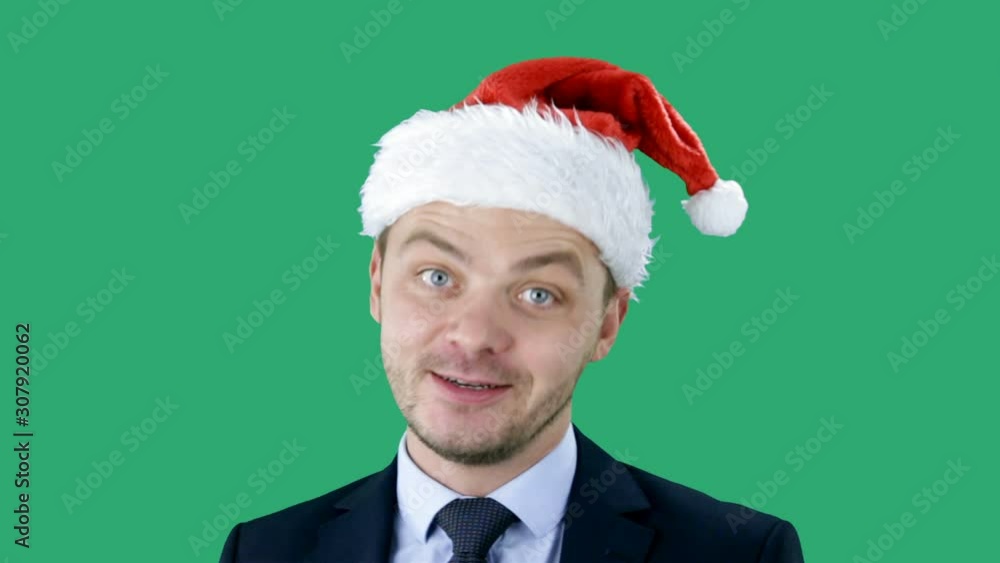 Young handsome caucasian guy in business suit and Santa hat stands on green background. Chroma key Young handsome caucasian guy in business suit and Santa hat stands on green background. Chroma key