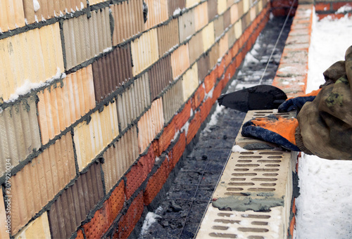 Worker in construction gloves lays a brick wall in the winter. winter building