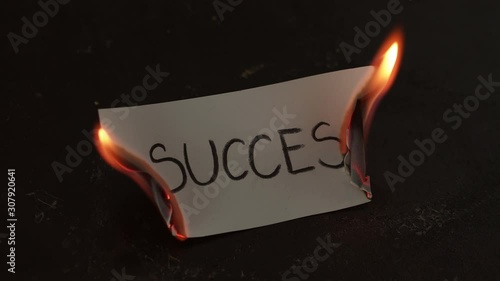 Success word written on white paper burns. Fire with smoke and ashes on black background photo