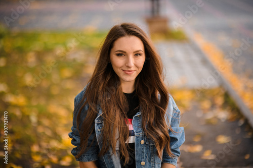 Portrait of a young woman standing on the paving stones with yellow leaves in the autumn park