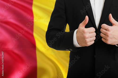 Guinea businessman showing thumbs up behind country flag with copy space. Successful international relations and agreement concept.