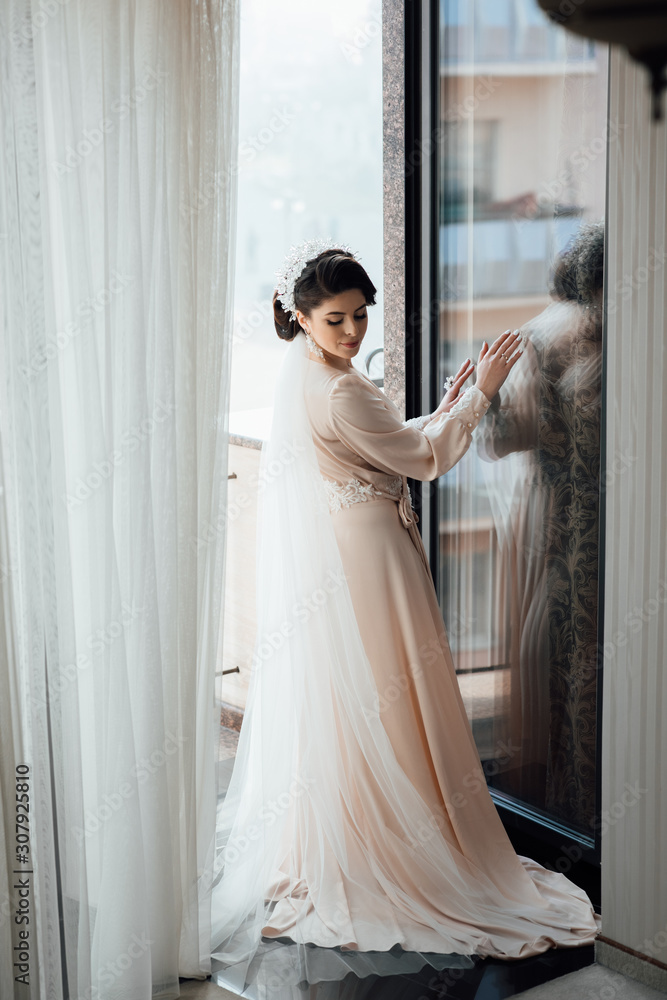 Young cute bride with beautiful hairdo morning at home in robe. The bride enters the balcony. Wedding style. Beautiful young bride with luxury wedding hairstyle. Young cute bride with beautiful hairdo morning at home in robe. The bride enters the balcony. Wedding style. Beautiful young bride with luxury wedding hairstyle.