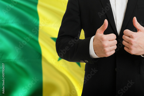 Senegal businessman showing thumbs up behind country flag with copy space. Successful international relations and agreement concept.