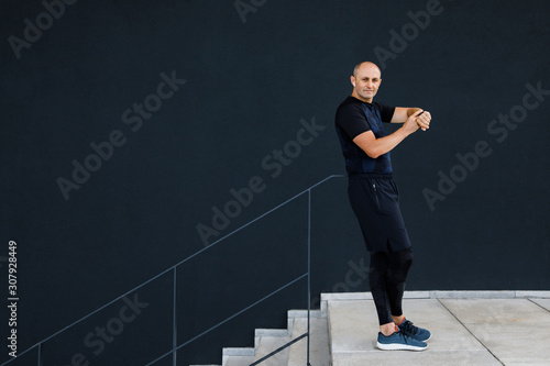 Young athletic man wearing sportswear doing his workout outdoors and looking at smart watch. Healthy Lifestyle