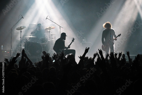 Concert shot, a huge crowd is standing in front of a lit stage clapping a band performance. © Martin