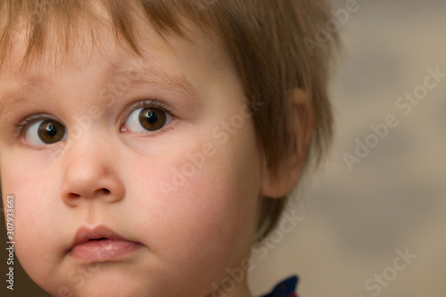 A cut-off portrait of a baby with big brown eyes and a surprised look. Selective focus. Copy space.