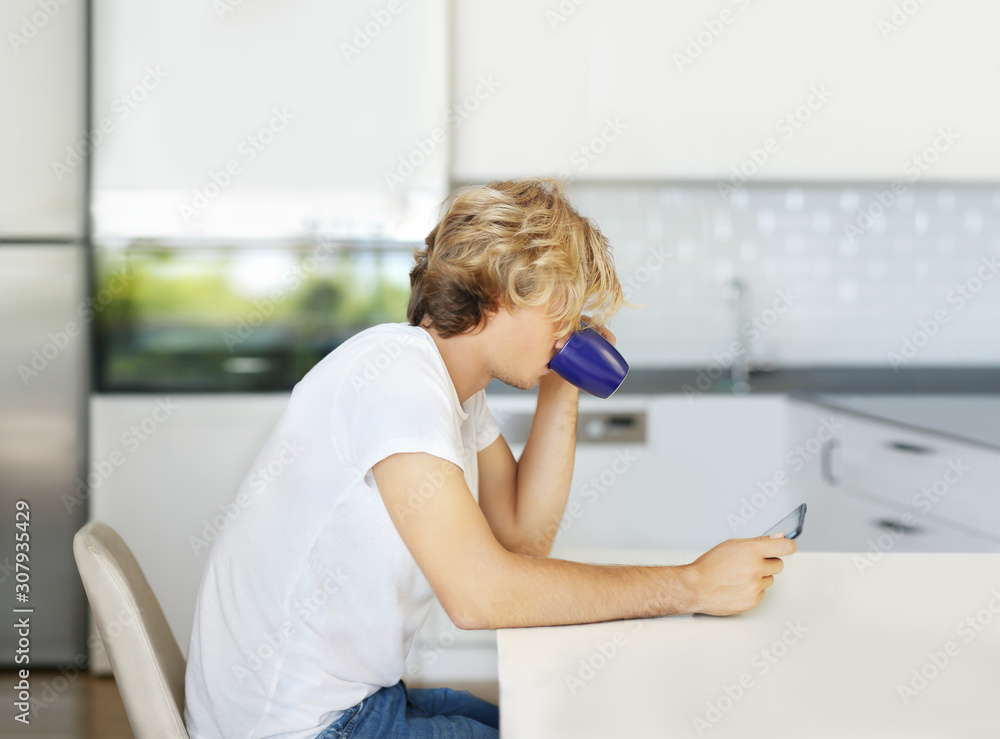 Teenage boy typing text message.Sitting in the kitchen.Using smart phone Teenage boy typing text message.Sitting in the kitchen.Using smart phone