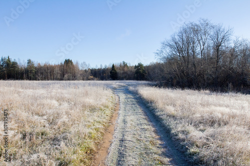 the road passes through the field covered with morning frost