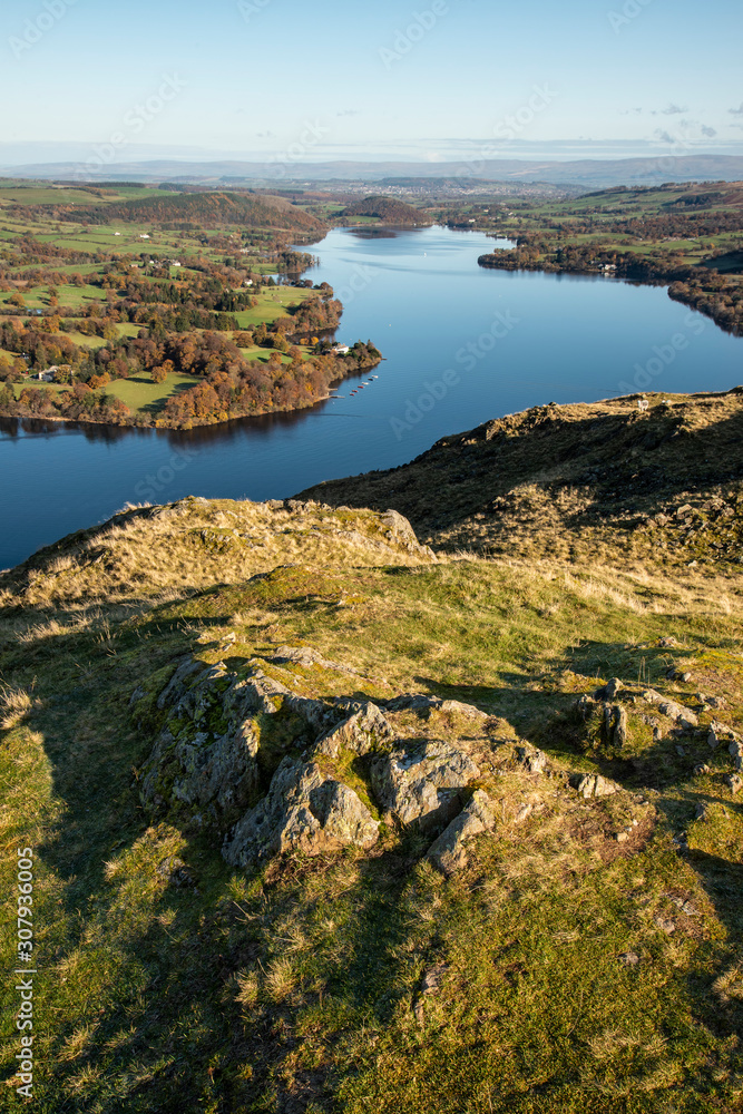 Obraz premium Beautiful Autumn Fall landscape of Ullswater and surrounding mountains and hills viewed from Hallin Fell on a crisp cold morning with majestic sunlgiht on the hillsides