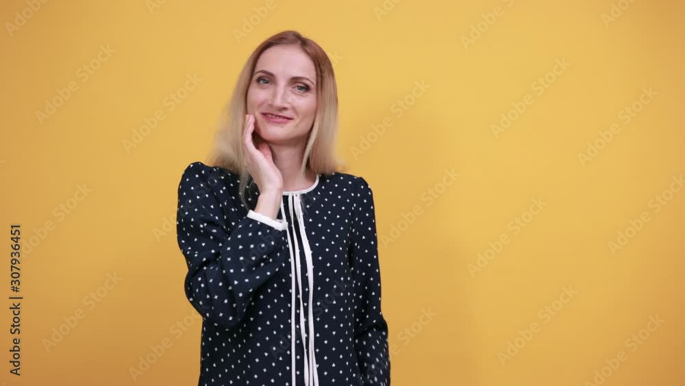 Charming caucasian young lady looking at camera, keeping hand on cheek over isolated orange background in blue shirt with white polka dot. Lifestyle concept Charming caucasian young lady looking at camera, keeping hand on cheek over isolated orange background in blue shirt with white polka dot. Lifestyle concept