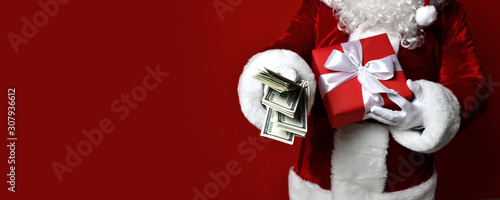 Santa Claus hold bunch of dollars money in one hand and red christmas gift box present