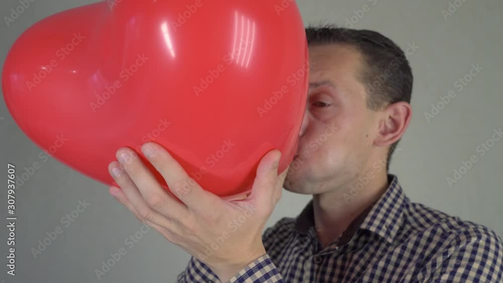 Funny man inflates a red heart-shaped balloon, concept of valentines day and love. Funny man inflates a red heart-shaped balloon, concept of valentines day and love.