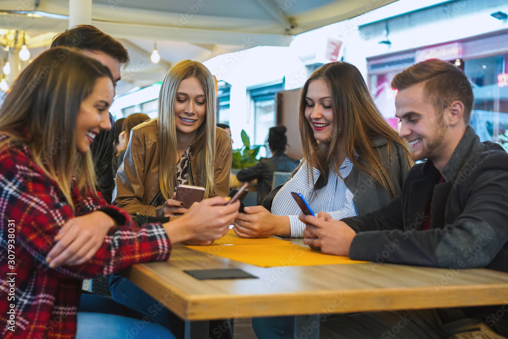 Group of teenagers gatherd in a bar using their smartphone- Friends sitting and doing chat, shareing photo, video, comments, likes on social media- Technology concept