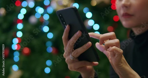 Asian woman using smartphone texting and shopping online while sitting near christmas tree at night.Technology communication business.close up shot.