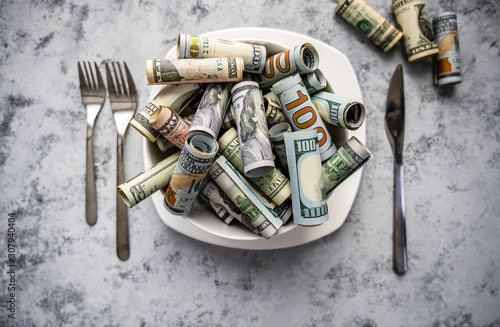 Banknotes of American dollar bills of various denominations are poured into a plate as a symbol of consumption of cash resources