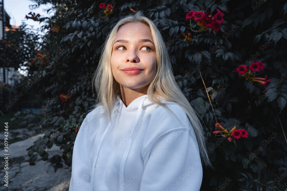 Sensual beautiful blonde girl with loose hair and red lips dressed in grey hoodie, tree with red little flowers on the background Sensual beautiful blonde girl with loose hair and red lips dressed in grey hoodie, tree with red little flowers on the background
