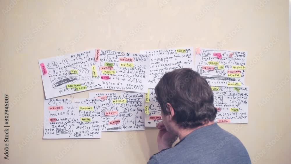 man works with various formulas and calculations on paper sheets that hang on the wall.research work. teacher in the workplace man works with various formulas and calculations on paper sheets that hang on the wall.research work. teacher in the workplace