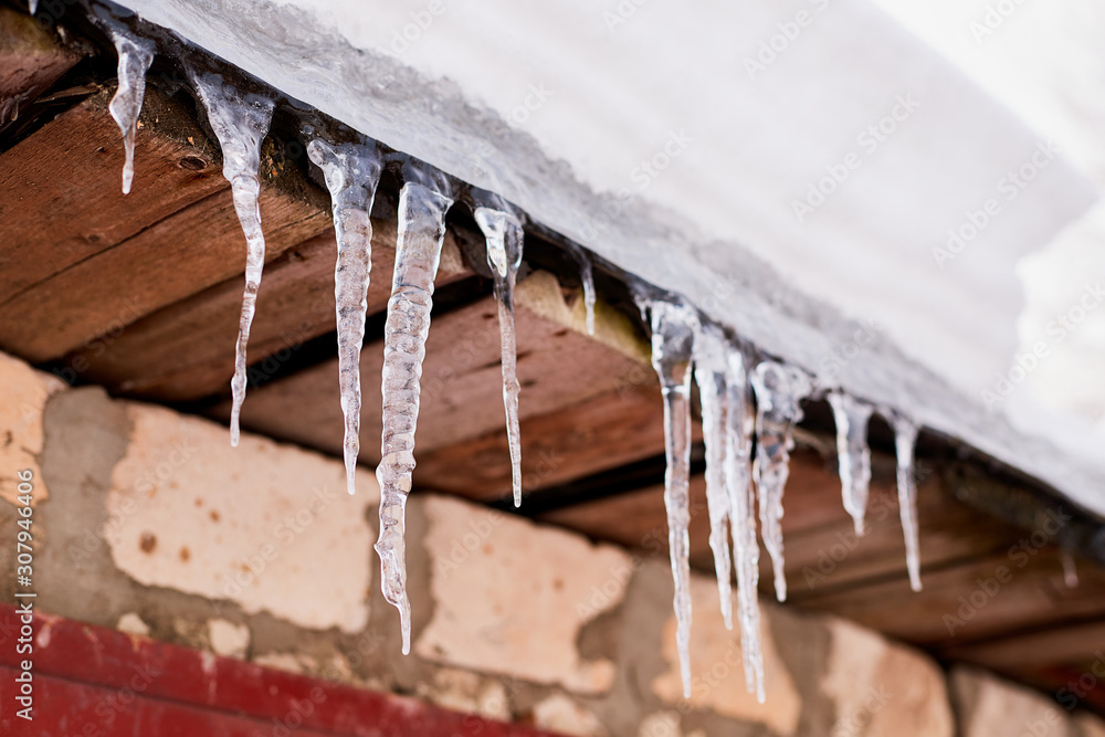 lots of white long icicles on visor of roof of wooden house in spring lots of white long icicles on visor of roof of wooden house in spring