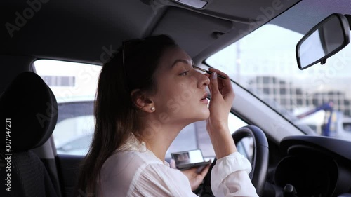 Eye brush, shadows, make-up in the car. A young woman looks in the mirror inside the car and applies make-up before a business meeting