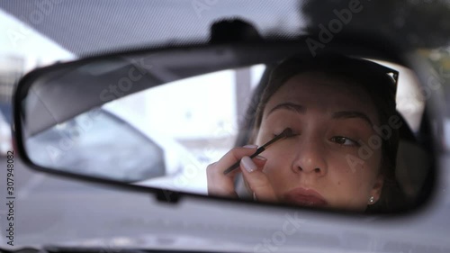 A beautiful Caucasian girl looks in the rear view mirror of the car and puts shadows on her eyes. Violation of the law in the car. A woman gathers in transport