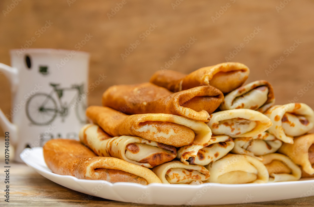 Pancakes with filling are a pyramid on a white plate standing on a wooden background close-up, in the background a Cup