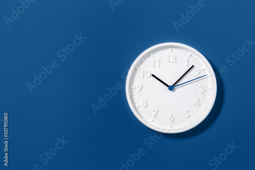 Big white plain classic wall clock on trending dark blue background. Ten o'clock. Close up with copy space, time management or school concept and summer standard or winter time change, opening hours.
