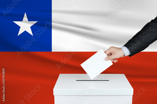 Election in Chile. The hand of man putting his vote in the ballot box. Waved Chile flag on background.