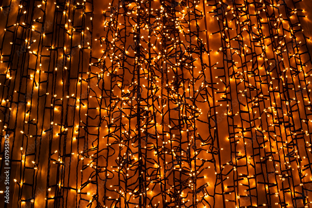  Festive Christmas orange lights. Glowing in the dark garlands on the wall. Golden lights of Christmas garlands on a dark background.