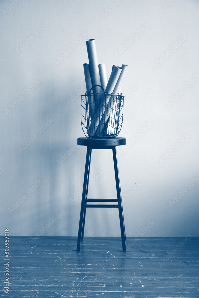 Classic blue color curly basket with rolls of brown Kraft paper on a high stool against a beige wall. Trendy color 2020. Classic blue color curly basket with rolls of brown Kraft paper on a high stool against a beige wall. Trendy color 2020.