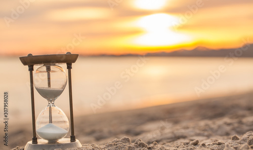 Hourglass in the sunset golden hour. Sand passing through the glass bulbs of an hourglass measuring the passing time as it counts down to a deadline or closure on a sunset/ sunrise beach background. 