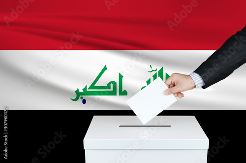 Election in Iraq. The hand of man putting his vote in the ballot box. Waved Iraq flag on background. photo