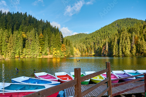 Multi-colored boats at the pier on Lake Lacu Rosu, Romania. Autumn landscape of mountain lake, forest and mountains.