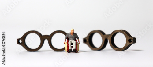 A miniature man in a wheelchair in front of two wooden miniature glasses. photo