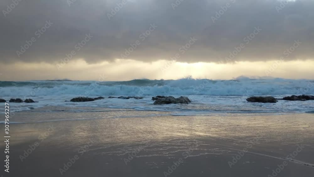 Waves gently washing and crashing across large rocks on a beach during sunrise Waves gently washing and crashing across large rocks on a beach during sunrise